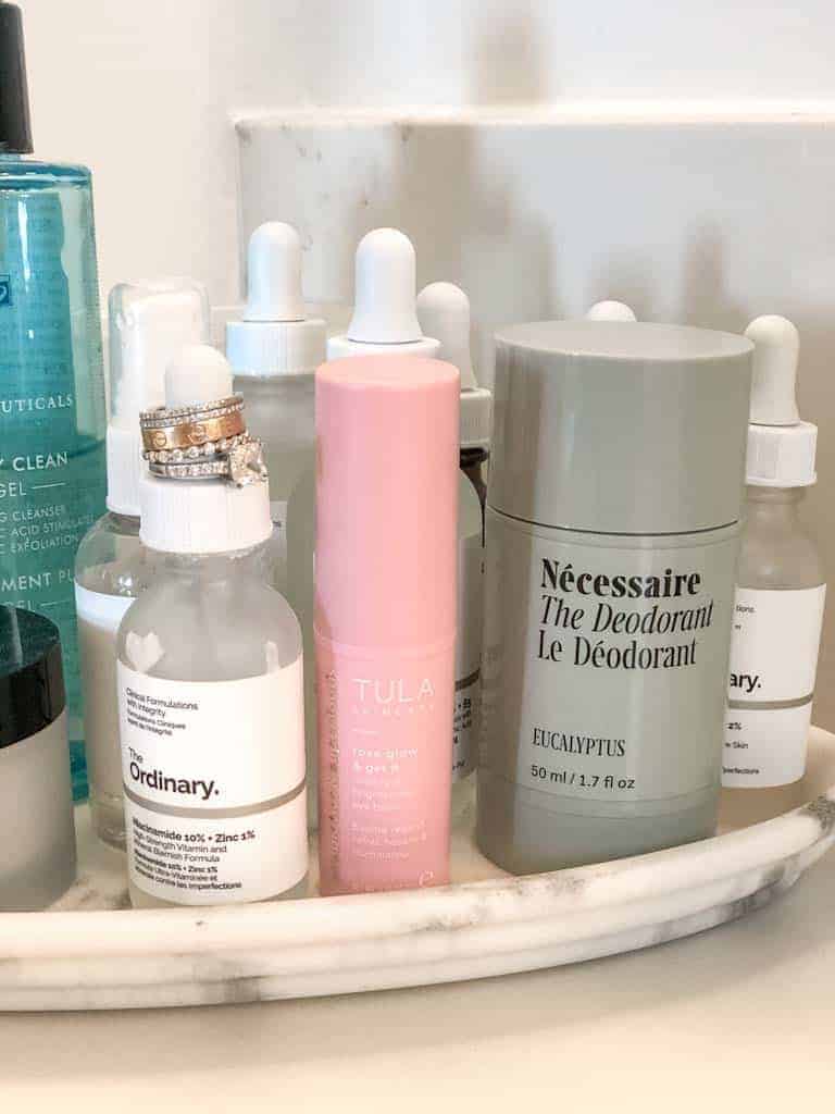 A list of nifty gifty 's from Signed Samantha and it includes this necessaire deoderant pictured on a marble holder and surrounded by the ordinary face products and tula skincare.