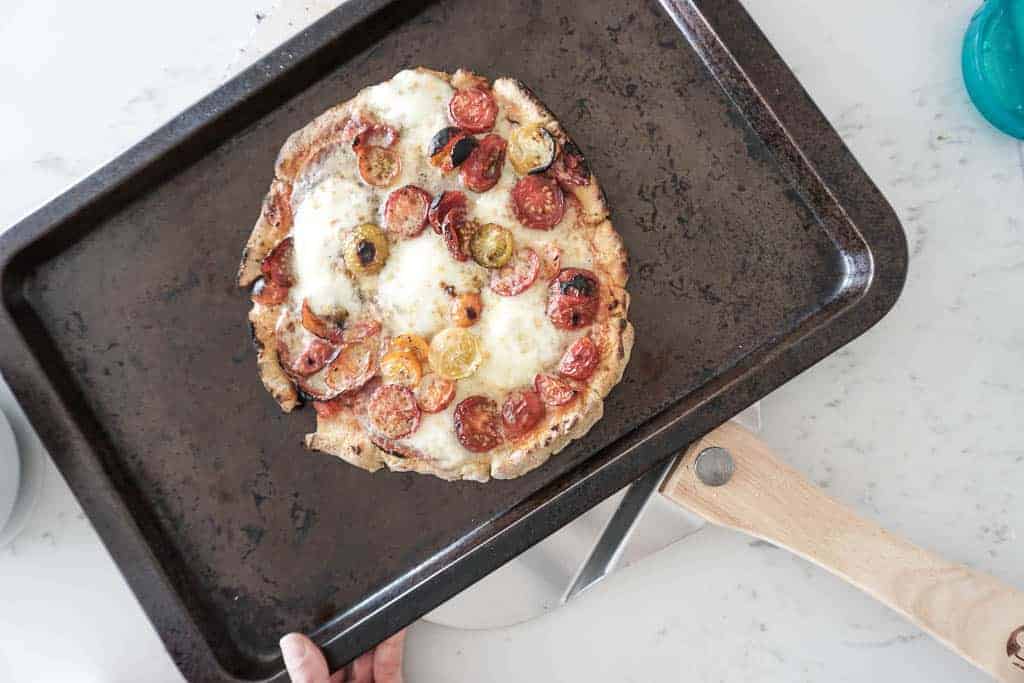 Signed Samantha's recipe for gluten free pizza crust - the cooked crust is pictured with tomatoes on a cheese pizza sitting on a baking sheet