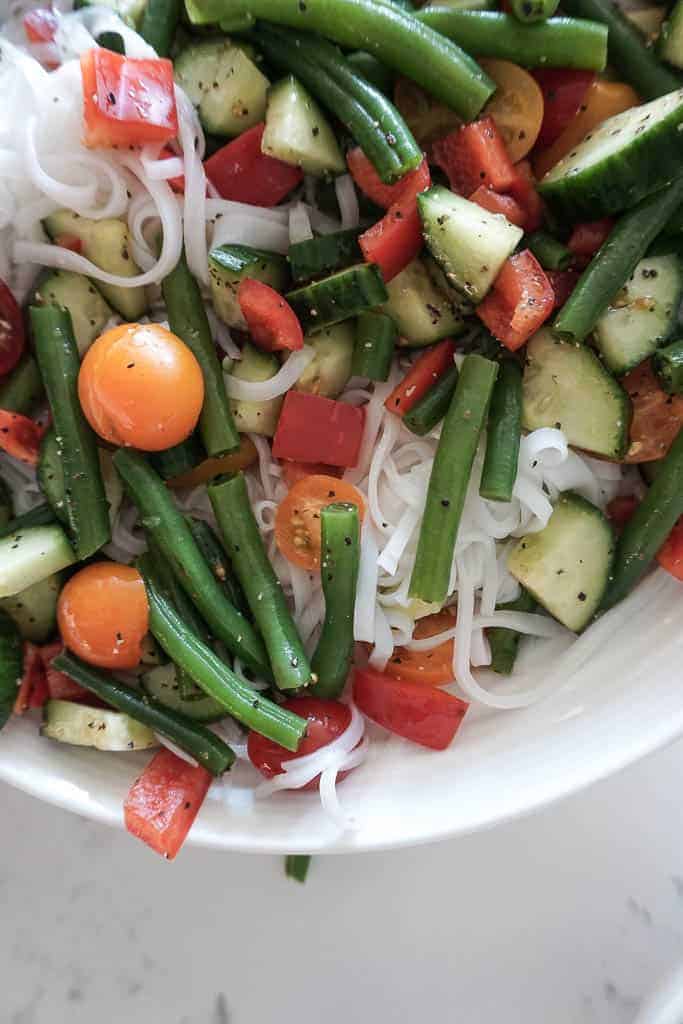 Signed Samantha's rice noodle salad with rice noodles, green beans, tomatoes, and red peppers in a bowl - it is a close up image so you can only see 1/4 of the bowl and the counter on the lower half of the image.