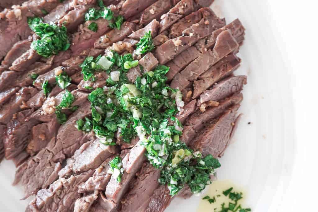 Signed Samantha' recipe for chimichurri on steak. There is an entire thinly sliced flank steak with a vibrant green chimmichurri sauce on top.