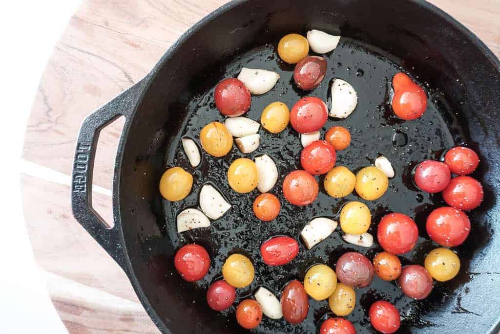 Signed Samantha's slow roasted tomatoes recipe - the tomatoes are pictured uncooked in a cast iron pan with garlic cloves.