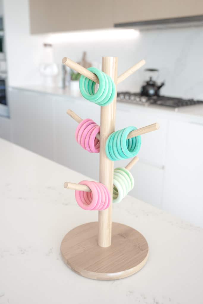 D.I.Y Ring Toss for Toddlers includes dollar store rings that are coloured different colours sitting on a wooden mug holder.