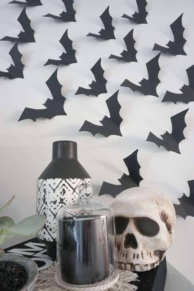 Signed Samantha's Halloween Bat decor on the wall behind a black and white vase, a black candle, and a faux skull.