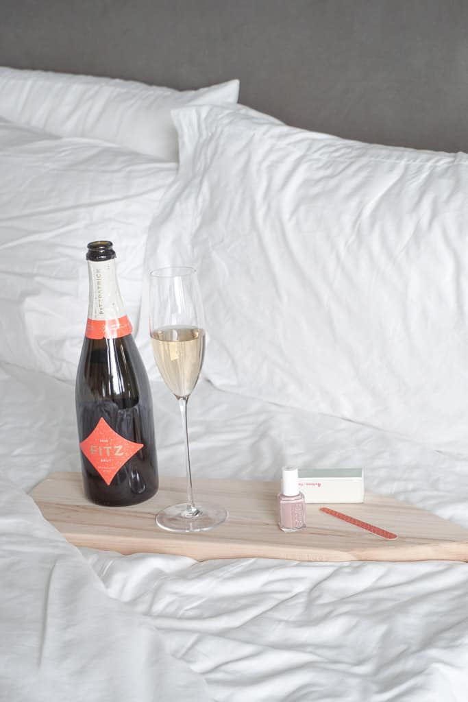 signed samantha goes over how to do self care during a pandemic which includes a bottle of champagne and nail polish as pictured on a wood serving board