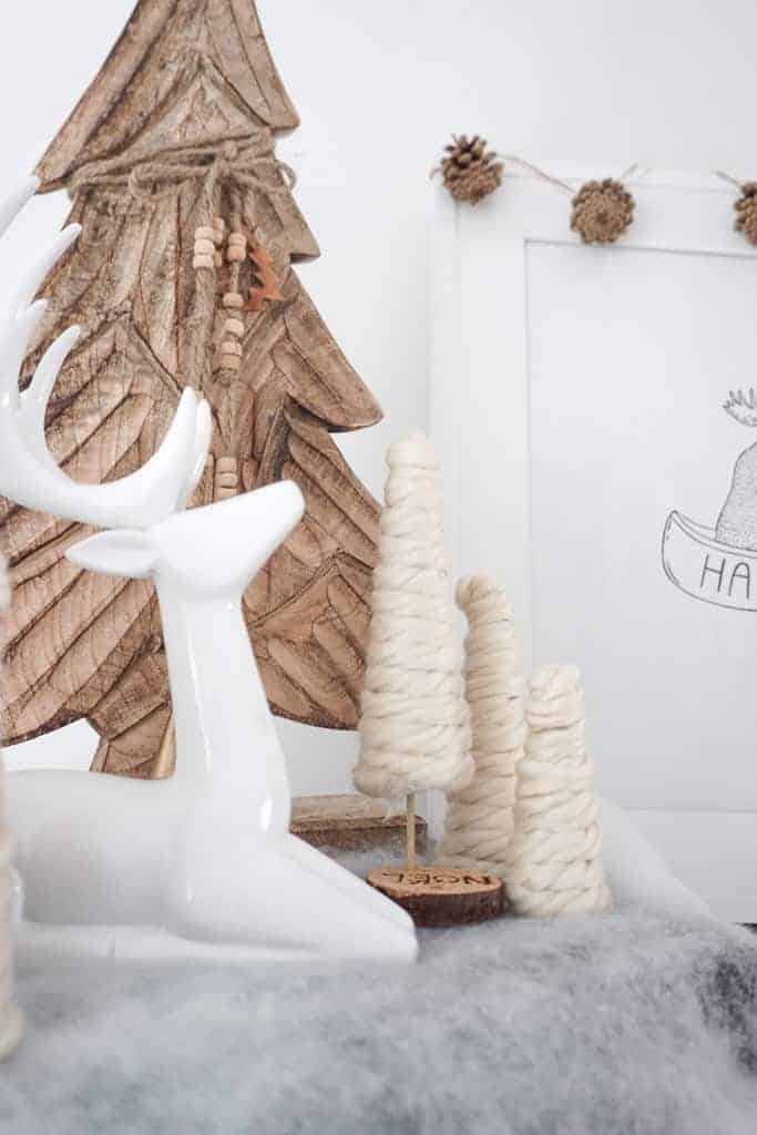 A white reindeer in the foreground with three D.I.Y mini Christmas trees behind and a wooden tree.