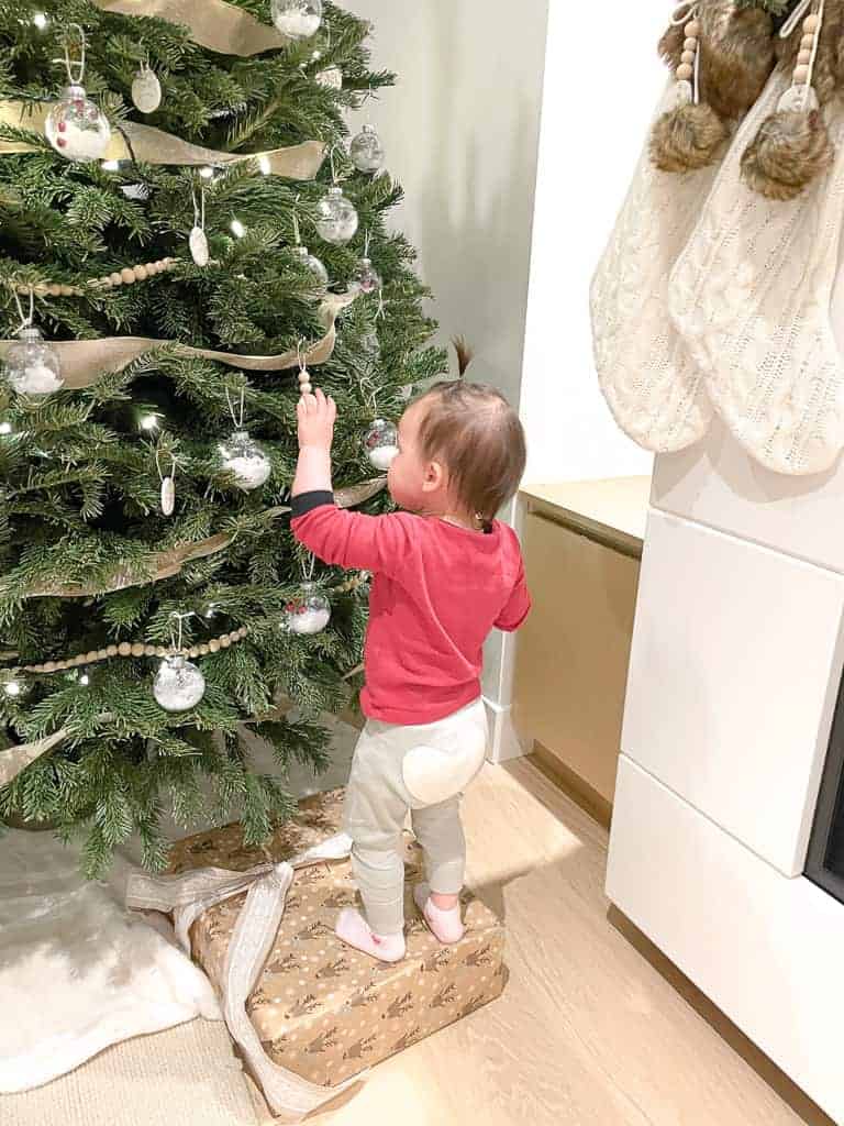 Signed Samantha's daughter is standing on top of a gift reaching for one of the D.I.Y Clay Ornaments on the Christmas tree