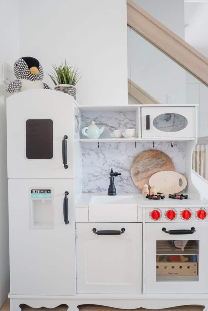 Signed Samantha Potter sharing her super simple way to do a kids kitchen makeover with her daughter, Sloane's kitchen. The kids kitchen that has red knobs, a faux marble backsplash, and black handles.