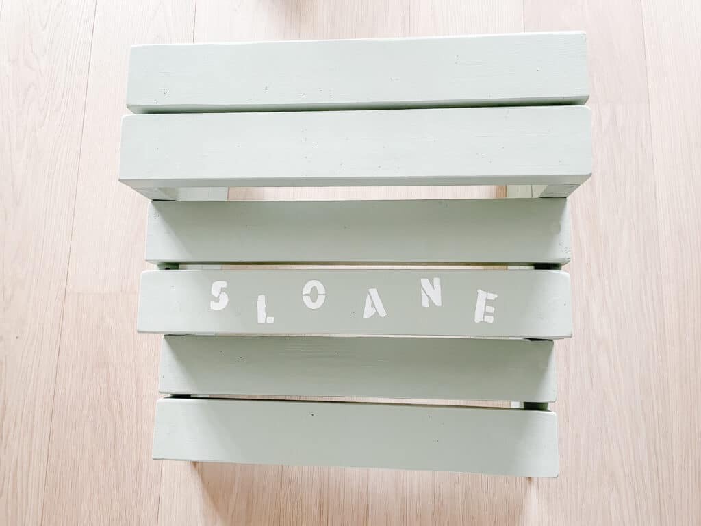 A sage green step stool for kids with Sloane's name on in it in white paint. Signed Samantha teaches you how to make your own step stool for kids.