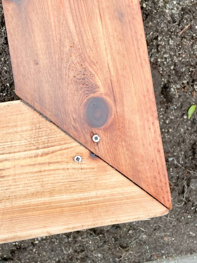 The corner of a garden box sitting outside in the garden bed. It is a black garden box with a non-painted cedar cap. this shows where the screw goes to get the cap on properly.