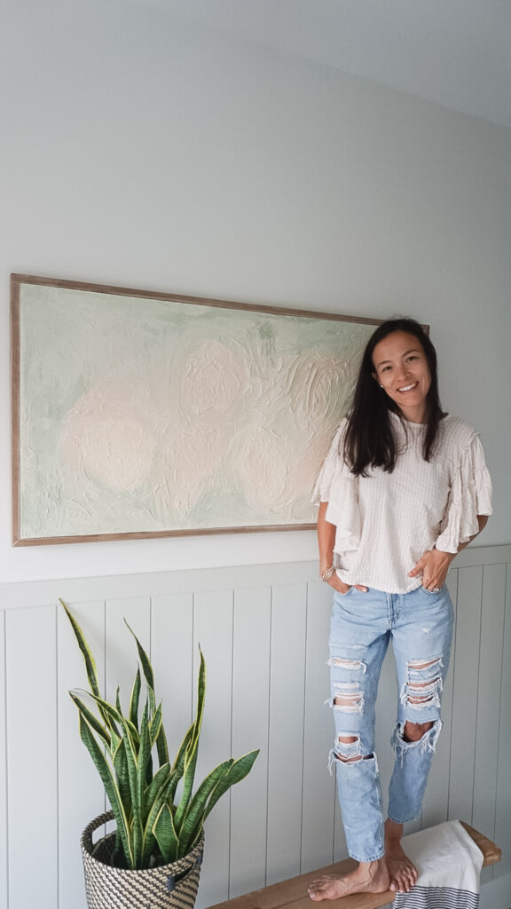 DIY Textured Art hanging on the wall above shiplap. The art contains green and pink colours. Very neutral-like. Signed Samantha is standing in front of it smiling