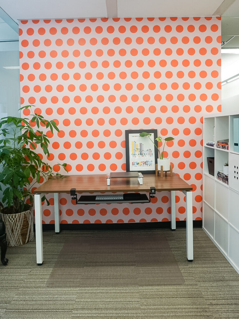Otto studio's peel and stick wallpaper in polka pop - tangerine is on the wall with a desk and laptop in front.