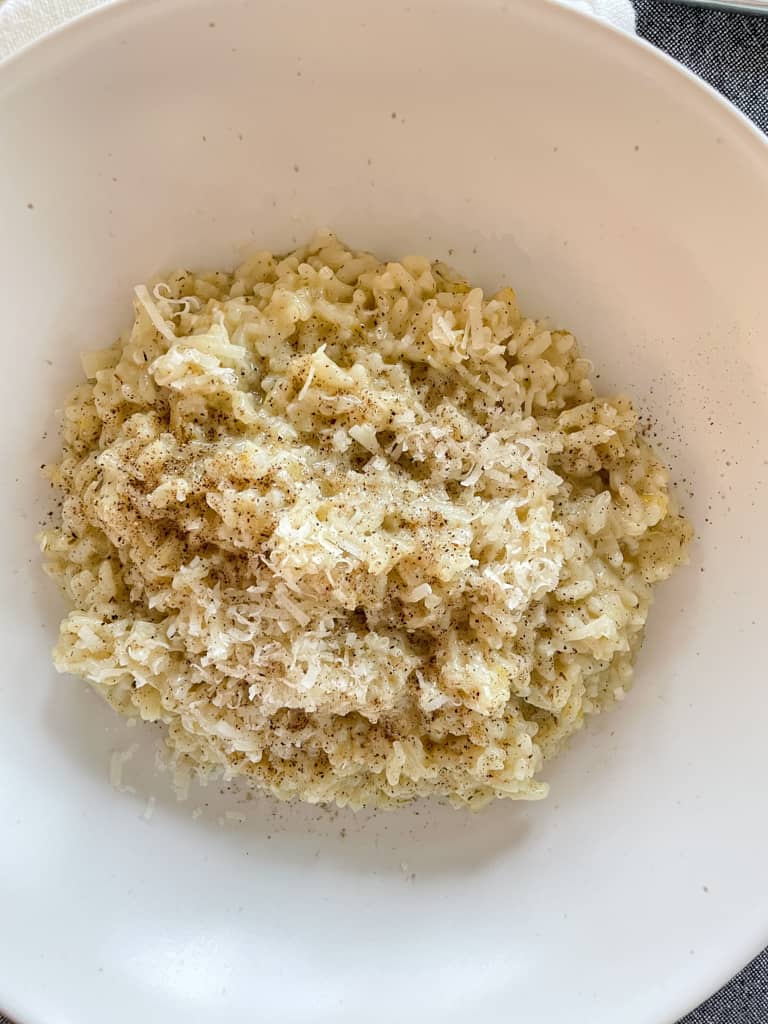 herb lemon instant pot risotto pictured in a white bowl with a fork and a dark grey napkin on the table around it.
