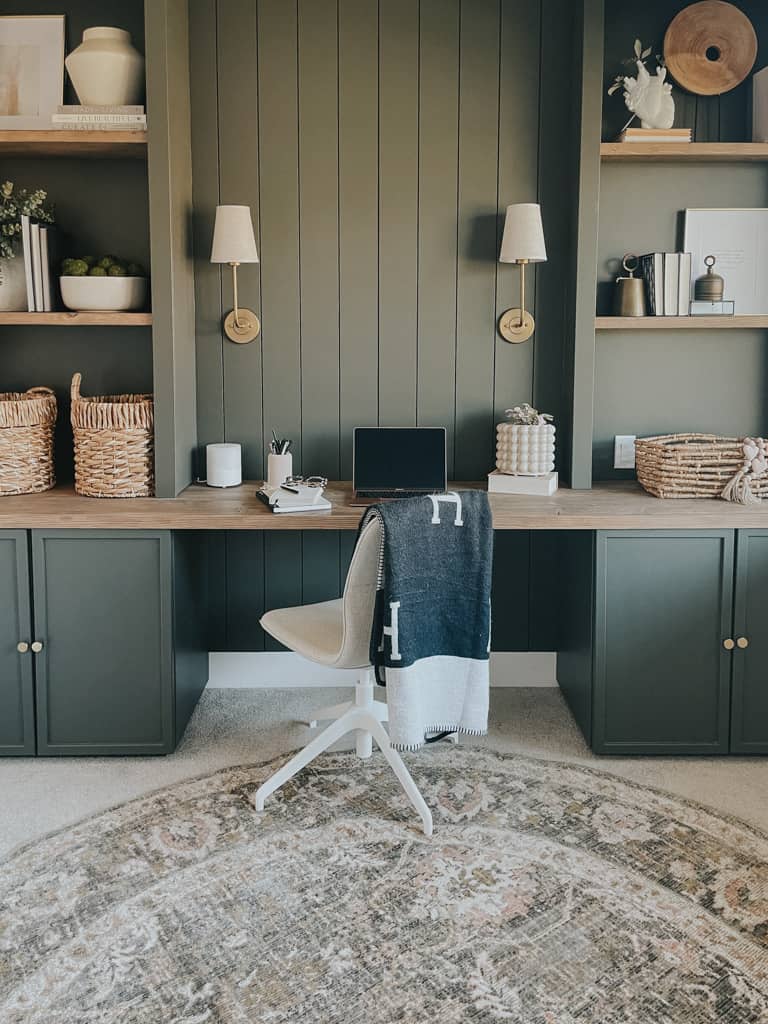 green home office with cabinets on the ground, a bookshelf above and a desktop in between. the green is a rich mossy green that compliments the cream of the office chair.