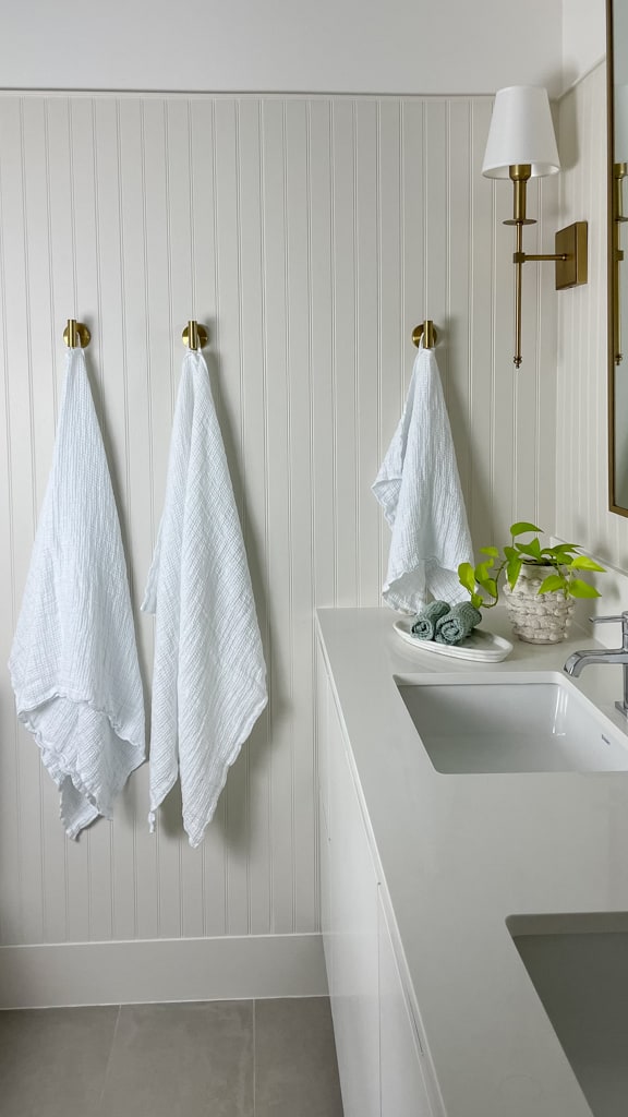 Flax Home linen waffle towels hanging up on gold hooks in a bathroom that has beadboard and a gold mirror