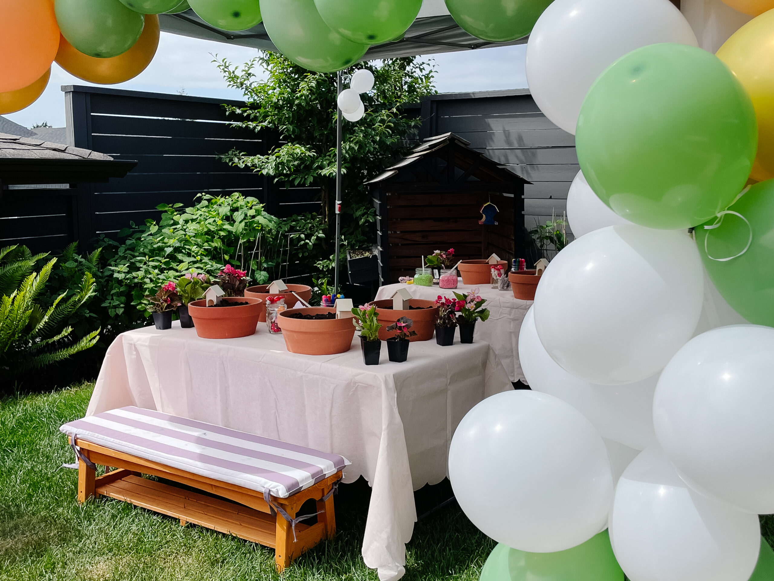a fairy garden birthday party set up with balloons, picnic tables and chairs, and fair gardens to make