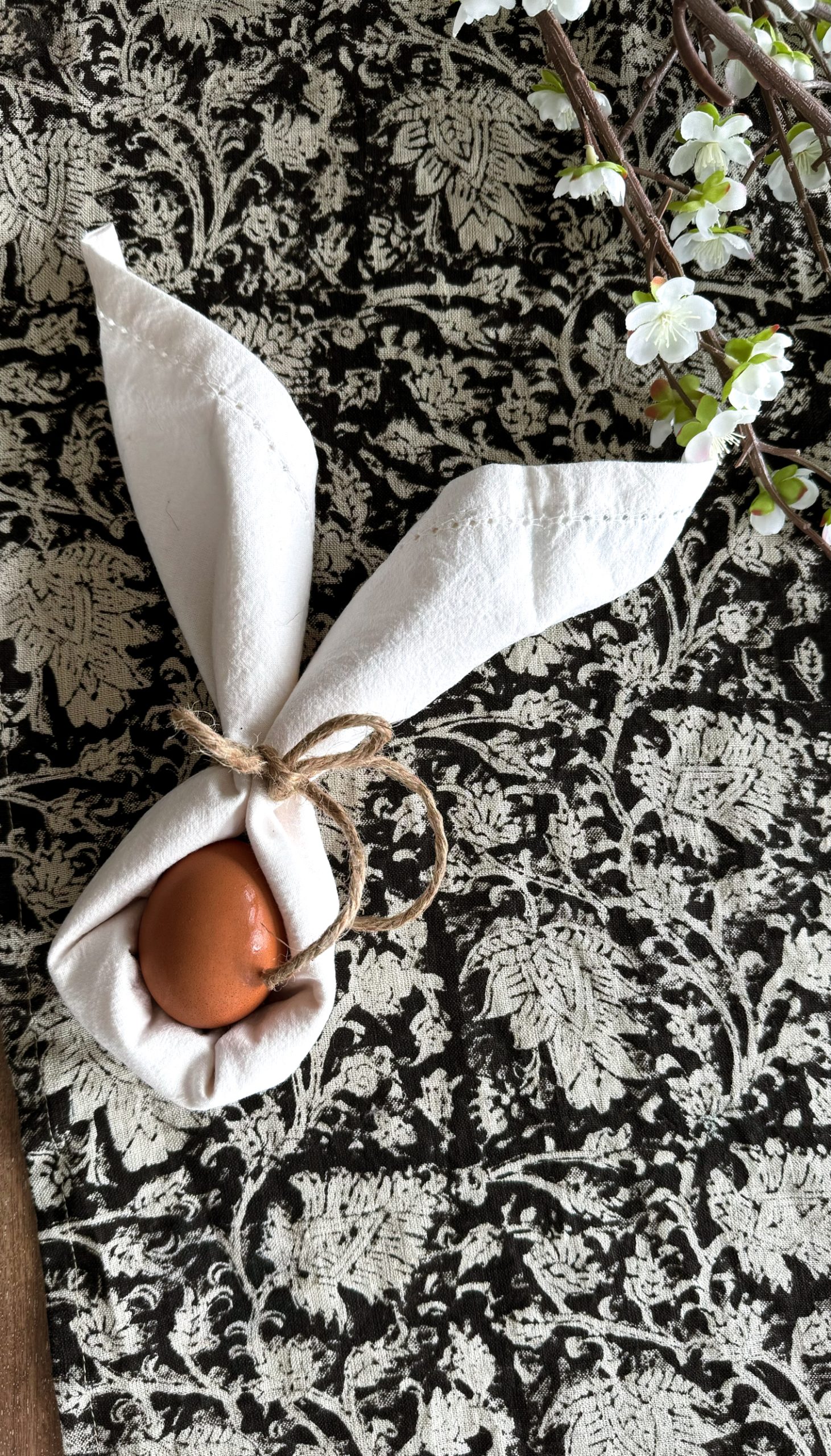 Easter bunny ear napkin fold with an egg sitting in the middle on top of a table cloth