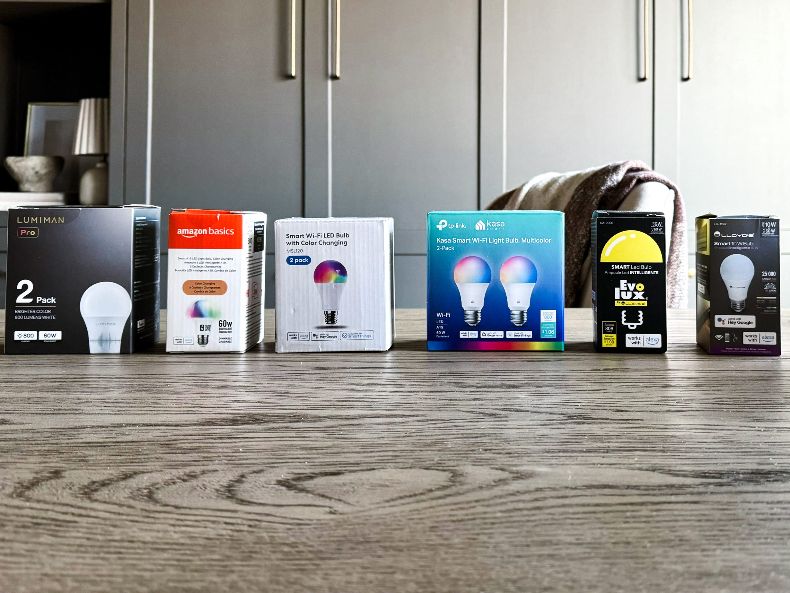 smart light bulb boxes lined up on top of a desk - reviewing them all